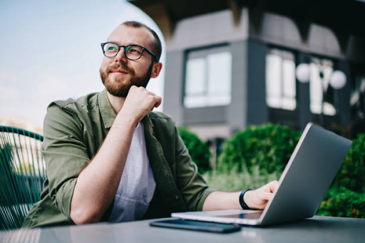 A freelancer with a laptop ponders in an outdoor setting, representing the freedom of working in Dubai.